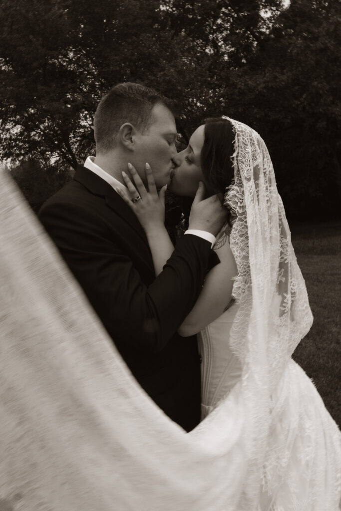 Bride and groom sharing a romantic kiss outdoors.