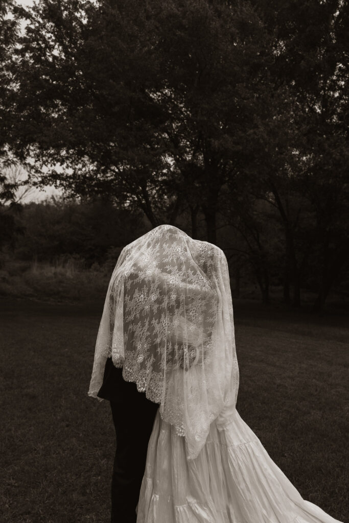 Sepia-toned photograph of a couple embracing under a lace veil outdoors.