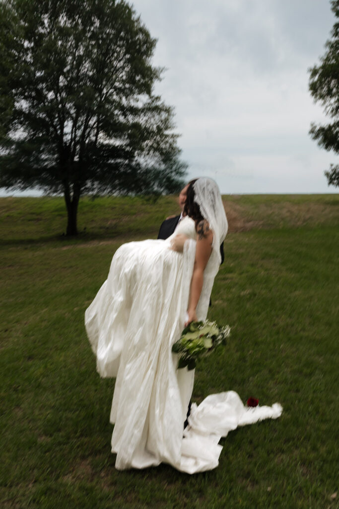 Groom carrying bride in white dress outdoors