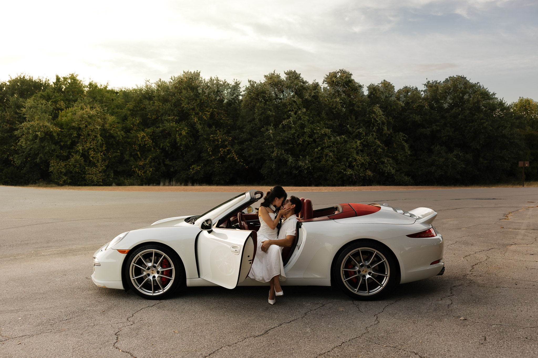 Couple embracing in a white convertible sports car against a wooded background