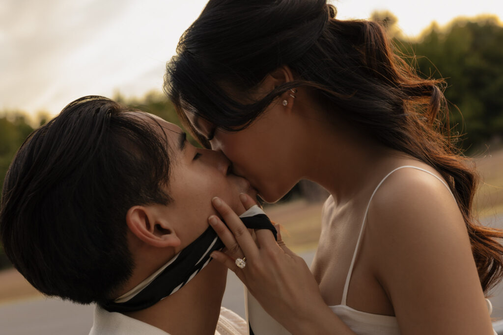 An engagement photo of a couple kissing, featuring a woman's hand with a diamond ring gently touching the man's face.