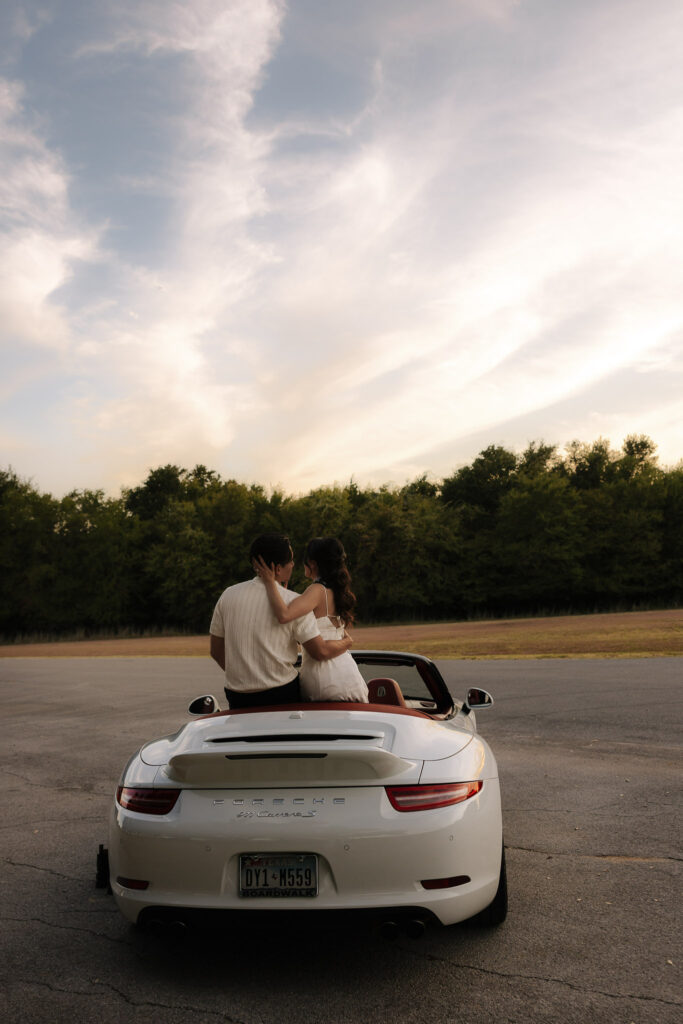 Couple embracing on a vintage car at sunset