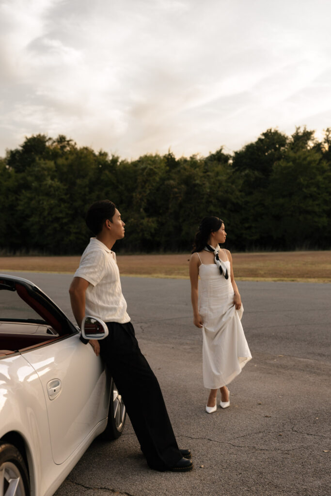 Couple in vintage attire with a white car, standing outside