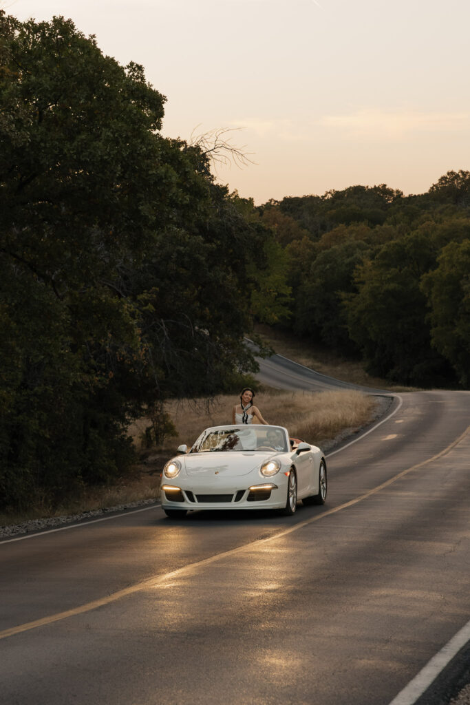 Woman standing in white convertible on country road during sunset