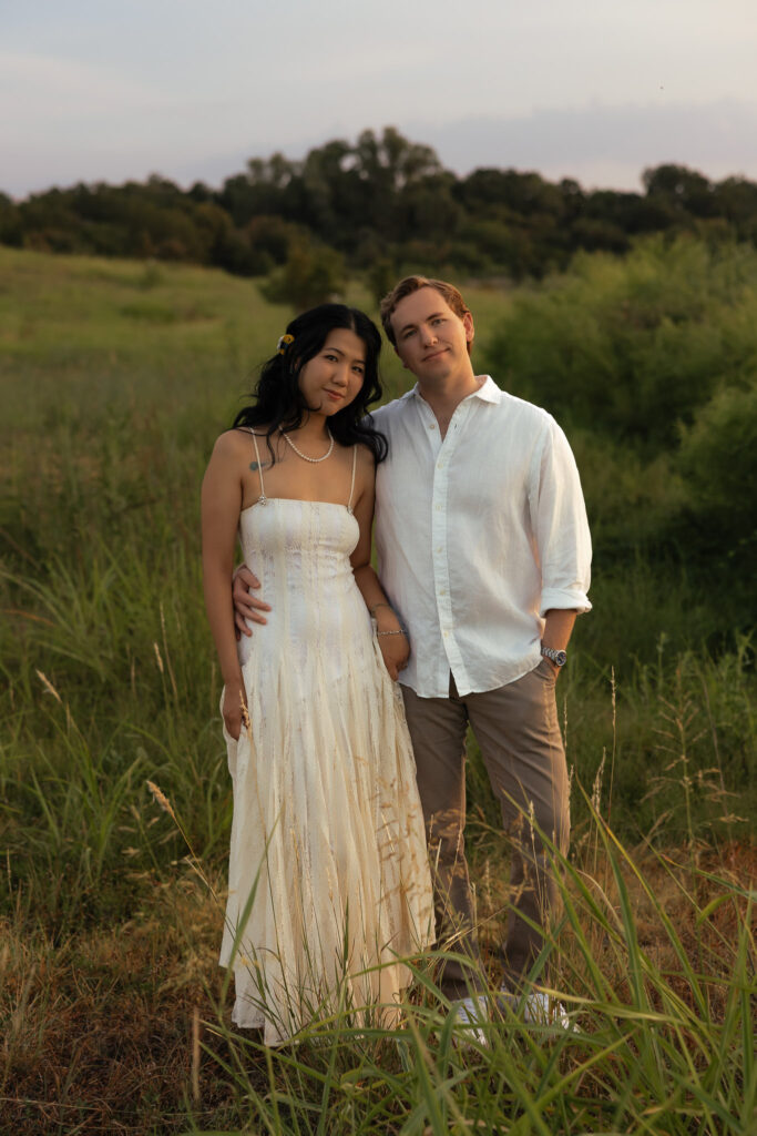 Couple posing together in a grassy field during sunset.