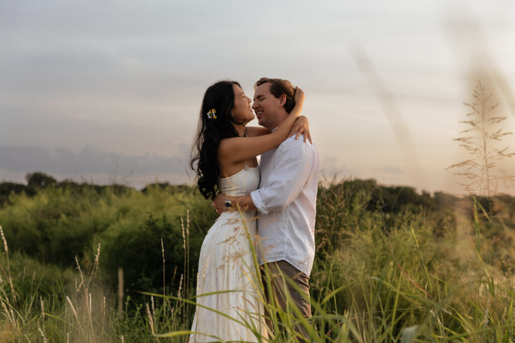 Couple embraces in a sunlit grassy field during sunrise.