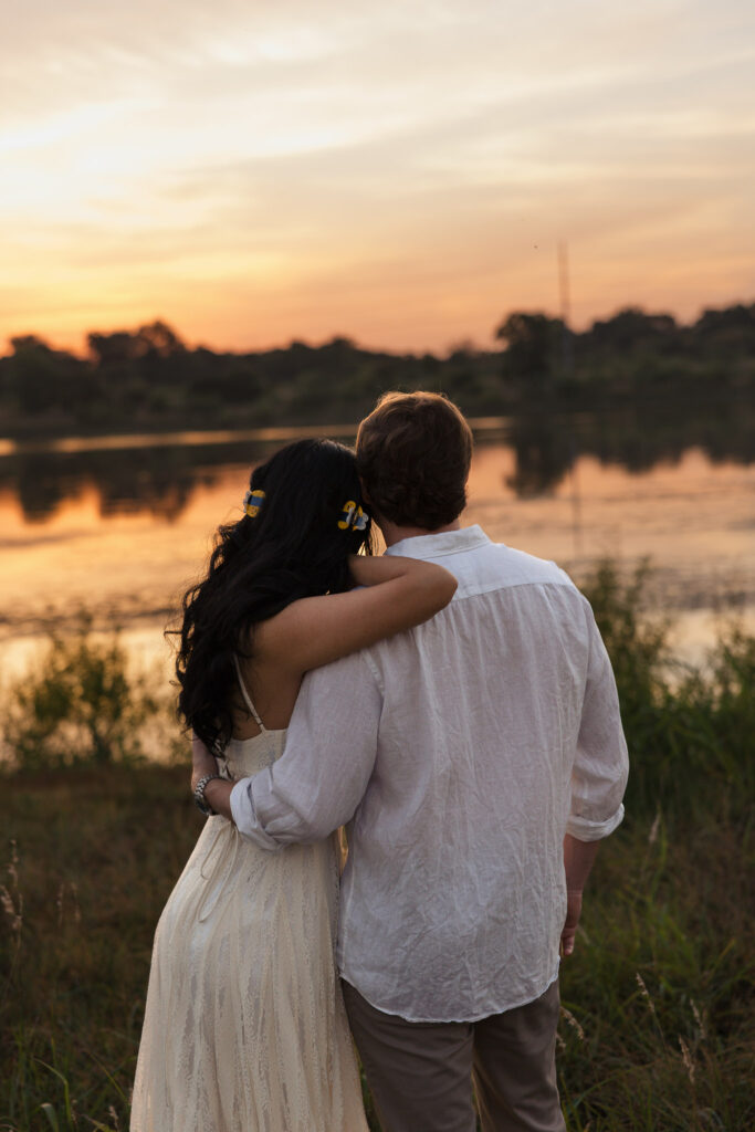Couple in white embracing by a lake at sunset