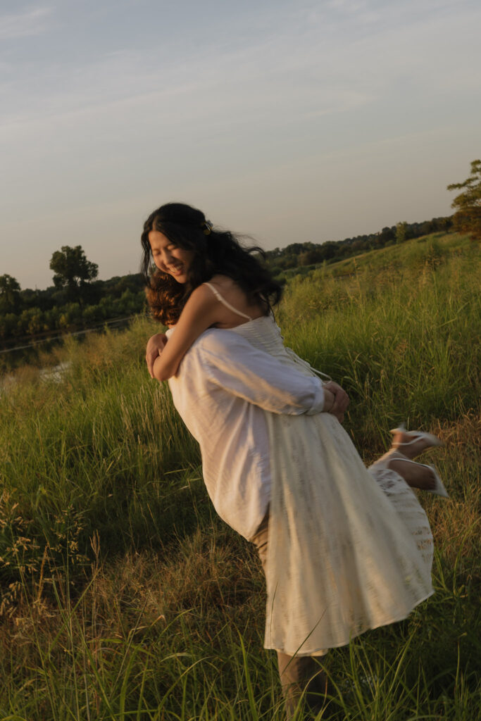 Couple embracing in a grassy field during a warm, golden sunrise.