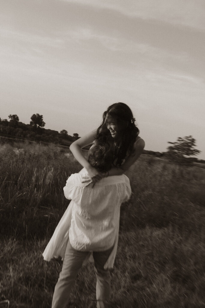 Couple embracing in a field at sunrise, sepia-toned image.