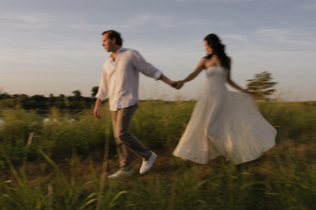 Couple walking hand in hand through a grassy field at sunrise
