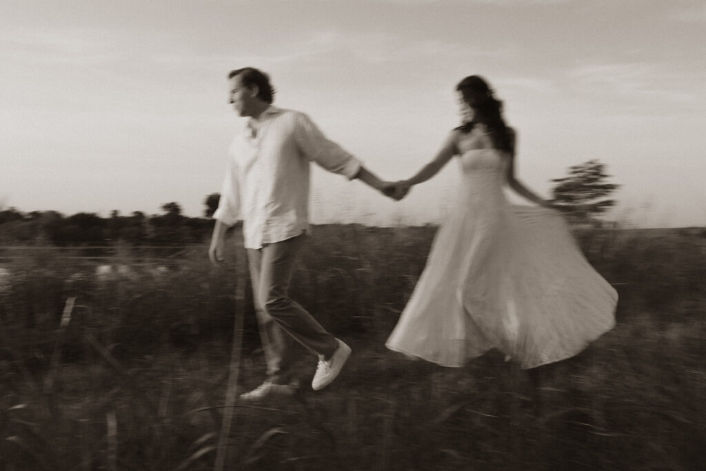 Couple holding hands while walking through a grassy field during sunrise.