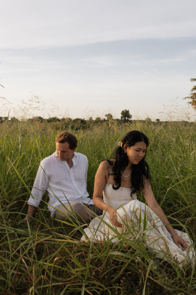 Engaged couple sitting in a grassy field at sunrise