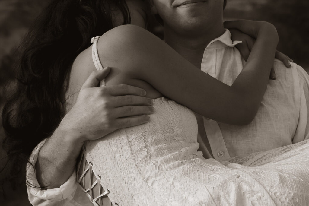 Close-up of a couple embracing, wearing light-colored attire.