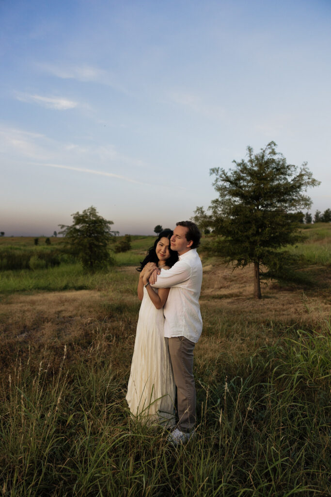 Couple embracing in grassy field at sunrise