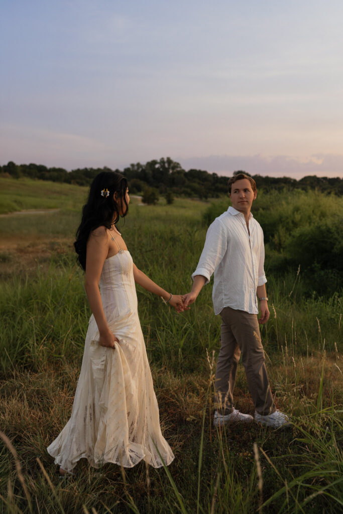Couple holds hands in a grassy field at sunrise